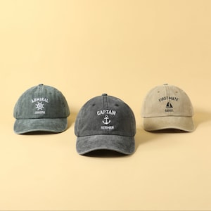 May include: Three different colored baseball caps with nautical themed embroidery. The caps are green, black, and beige. The green cap says "Admiral Joseph" with a ship's wheel. The black cap says "Captain Herman" with an anchor. The beige cap says "First Mate Daniel" with a sailboat.