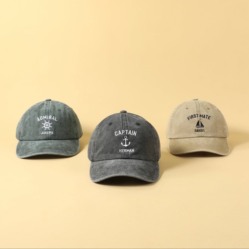 May include: Three different colored baseball caps with nautical themed embroidery. The caps are green, black, and beige. The green cap says "Admiral Joseph" with a ship's wheel. The black cap says "Captain Herman" with an anchor. The beige cap says "First Mate Daniel" with a sailboat.