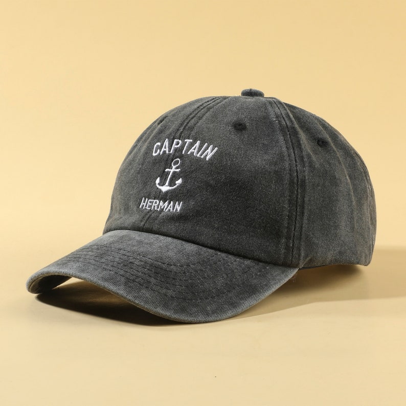 May include: A black washed cotton baseball cap with white embroidery that reads "CAPTAIN" with an anchor symbol and "HERMAN".
