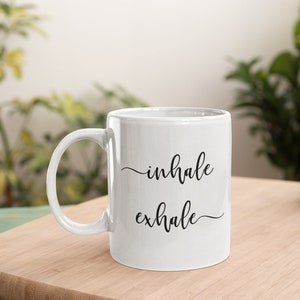 May include: White ceramic coffee mug with black text that reads "inhale exhale".