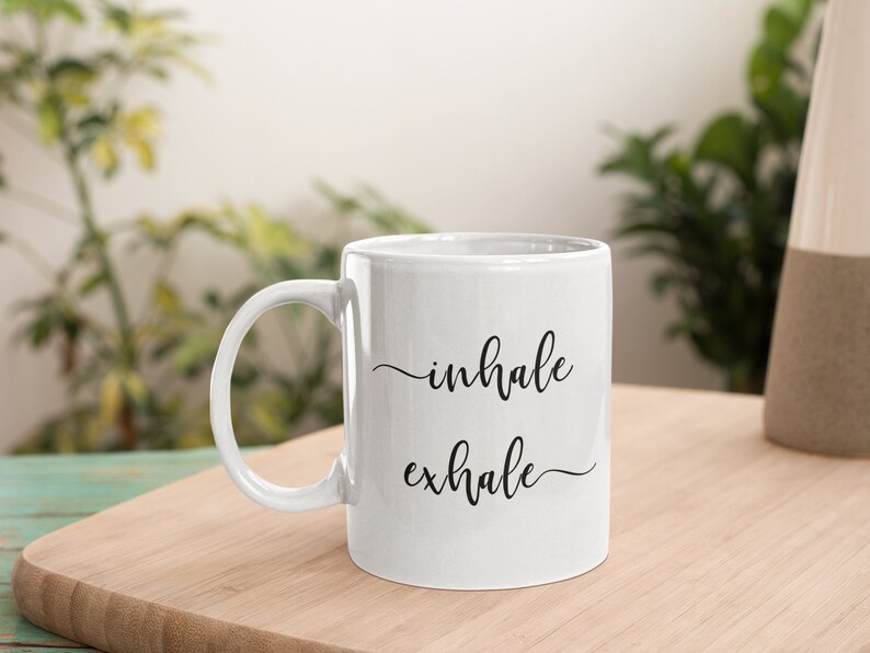 May include: White ceramic coffee mug with black text that reads "inhale exhale".