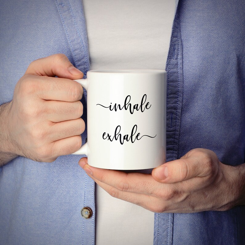 May include: White ceramic coffee mug with black text that reads "inhale exhale".
