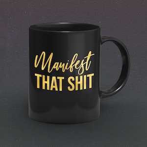 May include: Black coffee mug with a gold inscription that reads "Manifest That Shit".