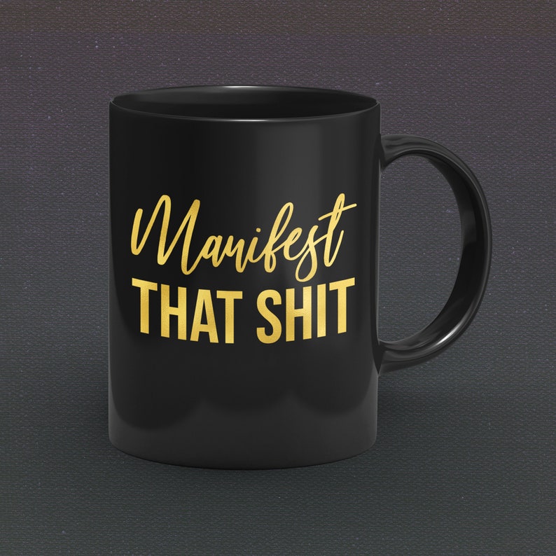 May include: Black coffee mug with a gold inscription that reads "Manifest That Shit".