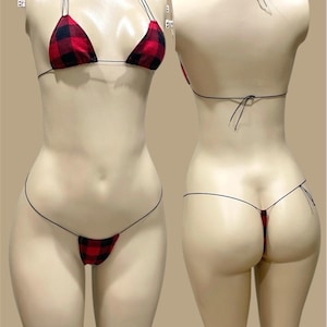 May include: A red and black plaid bikini set on a mannequin. The set features a triangle top with thin straps and a matching thong bottom. The bikini is made of a fabric with a classic plaid pattern.