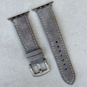 May include: Two gray leather watch bands with a light gray stitching detail. The bands have a metal adapter for an Apple Watch.