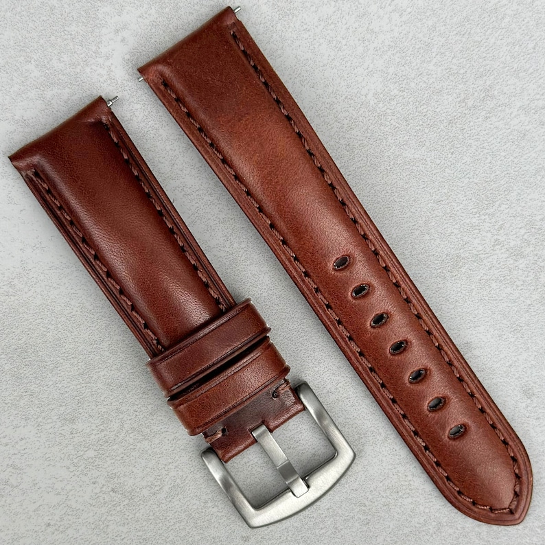 May include: Two brown leather watch straps with stitching. One strap has a silver buckle and the other has a silver keeper.