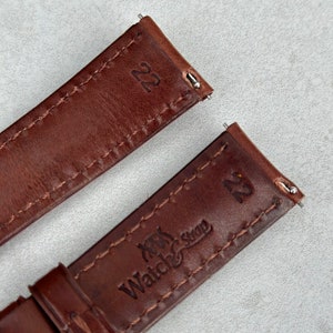 May include: Two brown leather watch straps with stitching. The strap on the top has the number "22" printed on it. The strap on the bottom has the text "Watch Strap" and the number "22" printed on it.