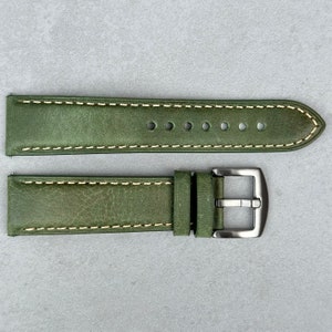 Könnte beinhalten: Ein grünes Lederarmband mit weißen Nähten und einer silbernen Schließe.