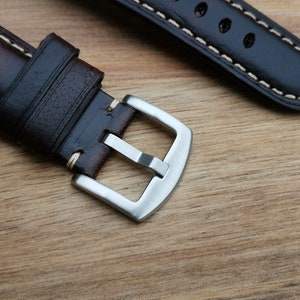 Close up of the brushed 316L stainless steel buckle on the Berlin brown leather apple watch strap. Strap placed on a wood background under natural lighting.