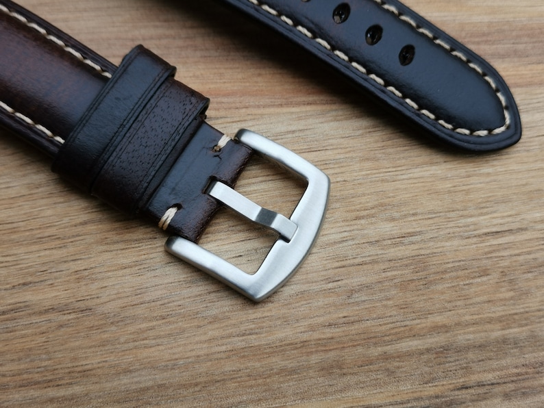 Close up of the brushed 316L stainless steel buckle on the Berlin brown leather apple watch strap. Strap placed on a wood background under natural lighting.