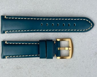 May include: A dark blue leather watch strap with white stitching and a gold buckle.