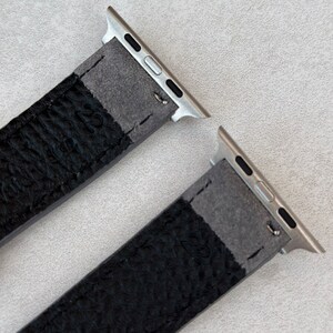 May include: Two black leather watch bands with silver metal connectors. The bands are designed for Apple Watches.