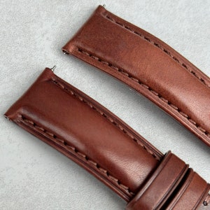 May include: Two brown leather watch straps with stitching. The straps have spring bars attached.