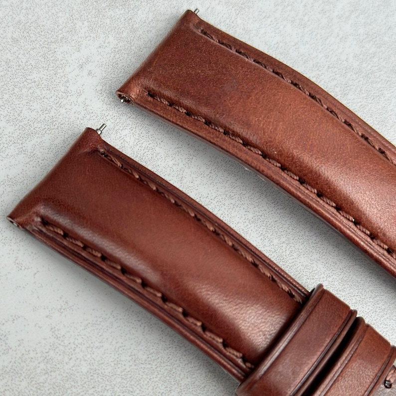 May include: Two brown leather watch straps with stitching. The straps have spring bars attached.