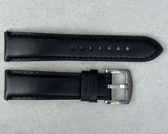 May include: Black leather watch strap with a silver buckle. The strap has stitching around the edges and multiple holes for adjusting the size.