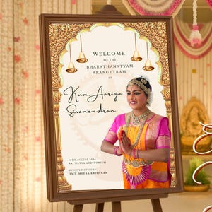 May include: A framed welcome poster on a wooden easel. The poster features a woman in traditional Indian attire, with text in English. The background is a decorated hall with floral garlands and the words "Entrance Welcome Poster".