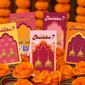 May include: A collection of greeting cards with the text "What Jhumka?" featuring gold-colored earrings. The cards are displayed with orange roses and colorful bangles, set against a backdrop of orange marigolds.