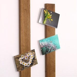 Könnte beinhalten: Zwei magnetische Holzleisten mit einer natürlichen Holzoptik. Die Leisten sind vertikal an einer weißen Wand montiert. Fotos werden mit Magneten an den Leisten befestigt.