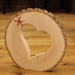 Może przedstawiać: Drewniany wycięty kształt serca w okrągłym kawałku drewna z czerwoną nicią zawiązaną wokół krawędzi.
