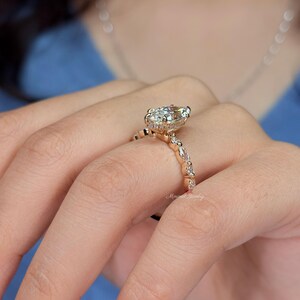 May include: A rose gold ring featuring a large pear-cut center stone and a band accented with alternating round and marquise-cut stones. The setting includes a hidden halo of small pav&eacute; stones beneath the main gem, with the text Minimal Jewelry.