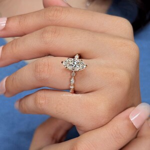 May include: A rose gold ring featuring a large marquise-cut center stone held by prongs. The band is adorned with a series of smaller round and marquise-cut stones set in a delicate, repeating pattern along the shank, creating a refined appearance.