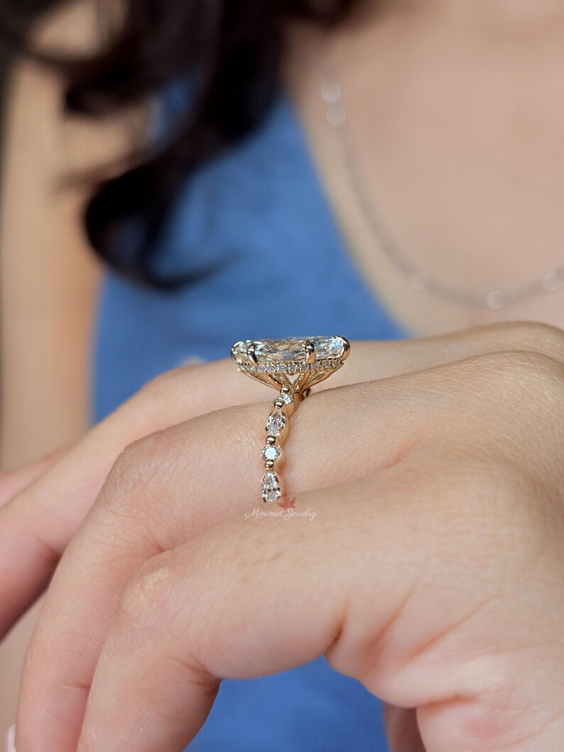 May include: A gold ring featuring a large, elongated marquise-cut center stone set horizontally. The band is adorned with a series of smaller, alternating round and pear-shaped diamonds, and a hidden halo of tiny stones encircles the base of the setting.