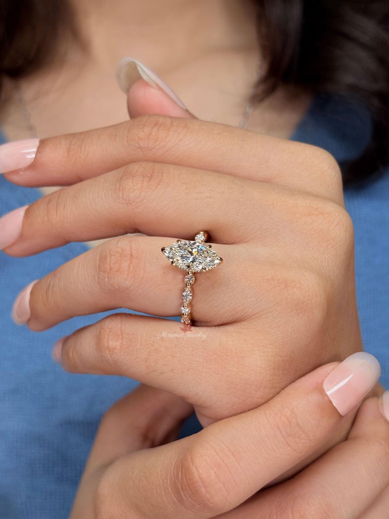 May include: A gold ring featuring a large marquise-cut center stone surrounded by smaller round and marquise-cut stones along the band. The metal has a warm, polished finish, and the design includes a delicate setting that highlights the stones.