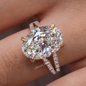 Op de afbeelding: Een gouden ring met een grote ovaal geslepen middensteen die door vier klauwen wordt vastgehouden. De ringband is gespleten in twee delen, elk bezet met kleine ronde pavé-diamanten. De tekst Minimal Jewelry is in rode letters op de ring zichtbaar.