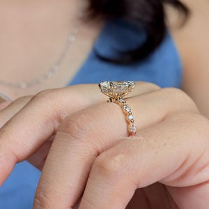 May include: A rose gold ring featuring a large oval-cut center stone surrounded by a halo of small round diamonds. The band is adorned with alternating marquise and round-cut diamonds, creating a detailed profile view of the setting.