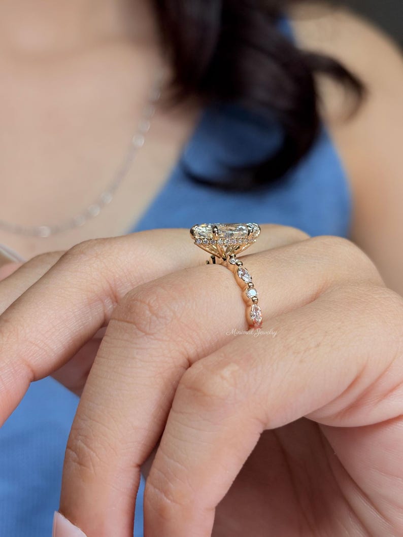 May include: A rose gold ring featuring a large oval-cut center stone surrounded by a halo of small round diamonds. The band is adorned with alternating marquise and round-cut diamonds, creating a detailed profile view of the setting.