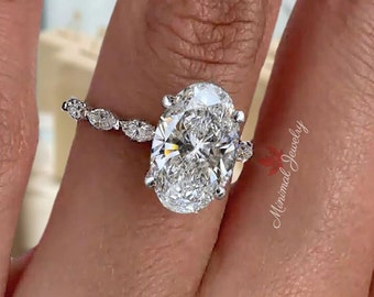 May include: A silver engagement ring with a large oval-shaped diamond and a pave diamond band. The ring is on a finger.
