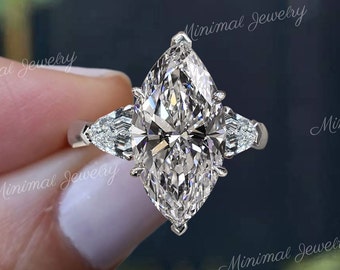 Könnte beinhalten: Ein Verlobungsring mit einem Marquise-Schliff-Diamanten und zwei kleineren birnenförmigen Diamanten an jeder Seite. Der Ring ist in einer Weißgoldfassung gefasst.
