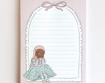 May include: A pink notepad with a decorative scalloped border and a bow at the top. The notepad features a lined interior and an illustration of a girl in a blue dress. The notepad is a stationery item.