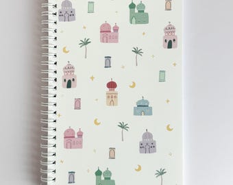 May include: A spiral-bound notebook with a cream-colored cover featuring a repeating pattern of colorful mosque illustrations, palm trees, crescent moons, and stars. The mosque designs include pink, green, and blue domes.