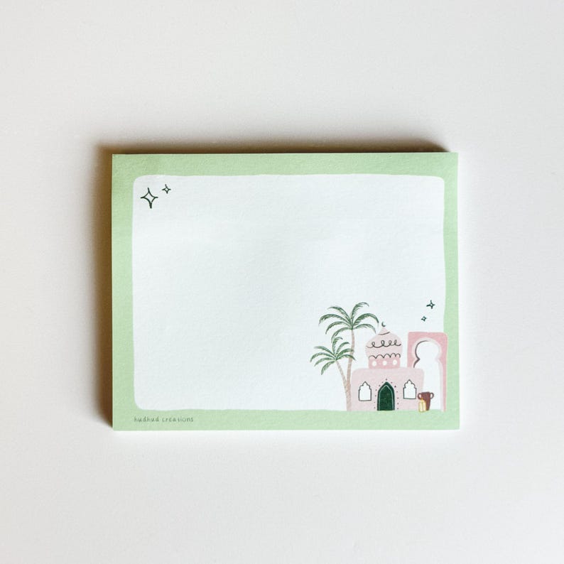 May include: A square notepad with a light green border and a white interior. The notepad features a whimsical illustration of a pink building with palm trees and a green door. Two stars are in the upper left corner. The text "badhad creations" is at the bottom.