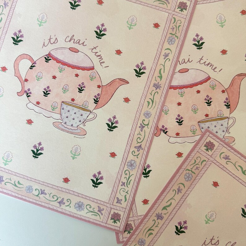May include: Watercolor illustration of a teapot and teacup with the text "it's chai time!". The teapot and teacup are pink with floral patterns. The background is a light beige with floral and decorative border elements.