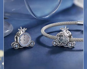 May include: Two silver-toned carriage charms featuring a crown topper and light blue stone accents. One charm is detached, displaying a clock face design, while the other is threaded onto a silver-toned mesh bracelet, showcasing a heart-shaped cutout.