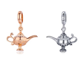 Puede incluir: Dos colgantes de plata con forma de lámpara de genio con detalles de cristal transparente. La lámpara de la izquierda es de color oro rosa.
