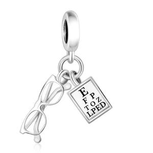 May include: Silver charm featuring a pair of eyeglasses and a miniature eye chart with the letters E, F, P, T, O, Z, L, P, E, D. The charm is designed to be attached to a bracelet or necklace, and is made of a shiny, reflective metal.