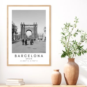 May include: Black and white photograph of an archway in Barcelona, Spain. The text "BARCELONA" is printed below the image, along with "SPAIN" and the coordinates "41.3851&deg; N, 2.1734&deg; E".