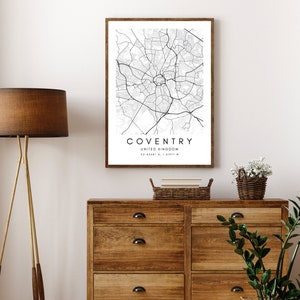 May include: A black and white map print of Coventry, United Kingdom, framed in a brown wood frame. The map shows the city's streets and landmarks. The print is hanging on a white wall above a wooden dresser.