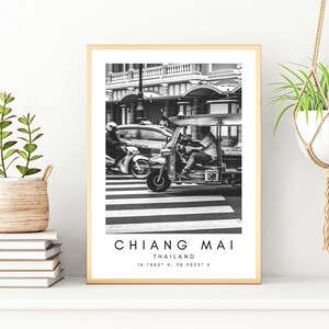 May include: Black and white photograph of a tuk-tuk driving down a street in Chiang Mai, Thailand. The text "CHIANG MAI THAILAND 18.7853&deg; N, 98.9953&deg; E" is printed below the image.