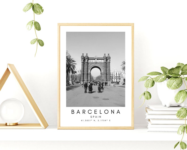 May include: Black and white photograph of the Arc de Triomf in Barcelona, Spain. The archway is made of stone and has a large arch in the center. There are people walking in front of the archway. The text "BARCELONA, SPAIN, 41.3851&deg; N, 2.1754&deg; E" is printed below the image.