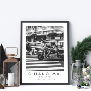 May include: Black and white photograph of a tuk-tuk driving through a crosswalk in Chiang Mai, Thailand. The text "CHIANG MAI, THAILAND, 18.7885&deg; N, 98.9855&deg; E" is printed below the image.