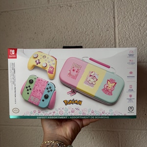 May include: A Nintendo Switch case and controller set with a Pikachu theme. The set includes a pink, yellow, and blue case, a yellow controller, and a pink and blue controller. The box has the text "Pokemon" and "Sweet Assortment".