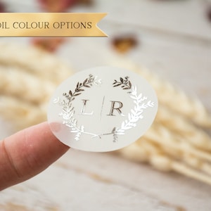 Peut inclure: Autocollant rond transparent avec un motif en feuille d'argent d'une couronne de feuilles et les lettres L et R à l'intérieur.
