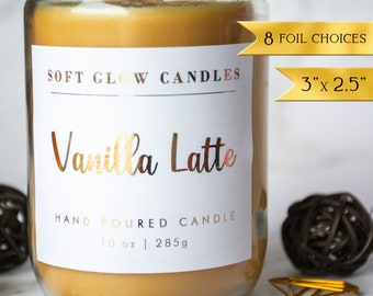 May include: A glass jar candle with a white label that reads "SOFT GLOW CANDLES" and "Vanilla Latte". The label also says "HAND POURED CANDLE" and "10 oz | 285g". There are two gold foil ribbons on the jar. One ribbon says "8 FOIL CHOICES" and the other says "3" x 2.5"".