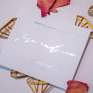 May include: A white card with silver foil lettering that reads "American Classics" and "fire and ice". The card is sitting on a white surface with gold diamond-shaped clips.