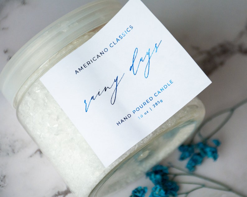 May include: A white glass jar with a white label that reads "Americano Classics Rainy Days Hand Poured Candle 10 oz | 285g".